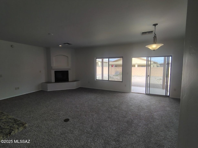 unfurnished living room with a fireplace with raised hearth, visible vents, dark carpet, and baseboards