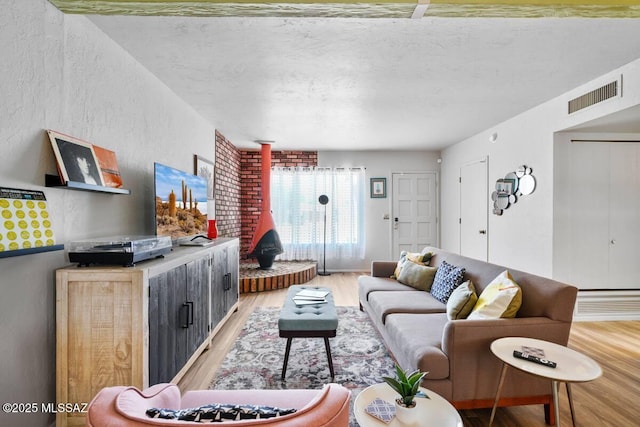 living room with a textured wall, a wood stove, light wood-type flooring, and visible vents