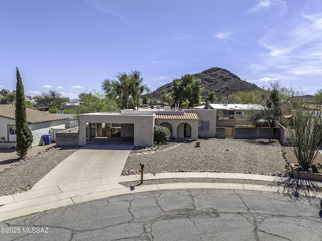 view of front facade featuring fence, stucco siding, an attached carport, concrete driveway, and a mountain view