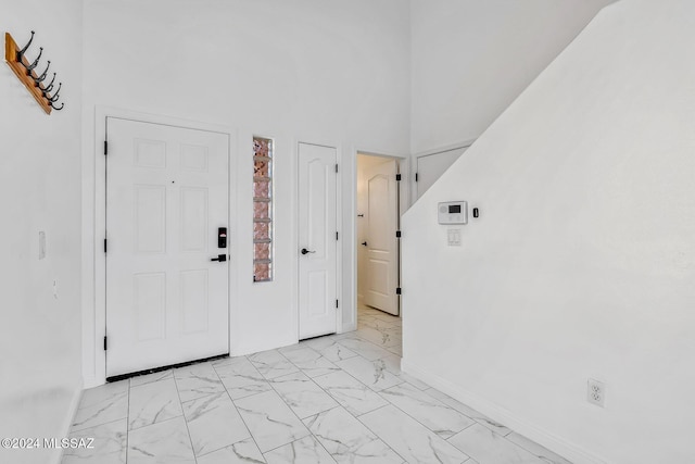 entrance foyer featuring marble finish floor, a high ceiling, and baseboards