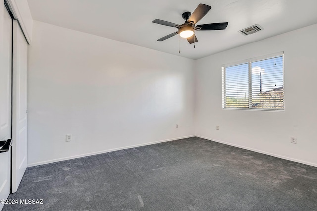 spare room with visible vents, baseboards, ceiling fan, and dark colored carpet