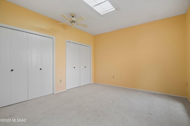 unfurnished bedroom featuring light colored carpet, baseboards, a ceiling fan, and multiple closets
