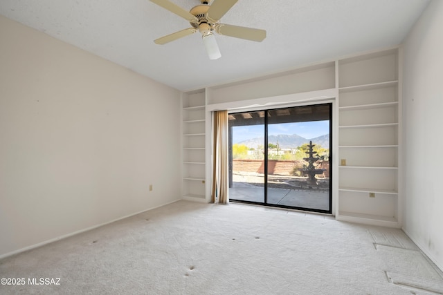 unfurnished room with a ceiling fan, built in shelves, carpet floors, baseboards, and a mountain view