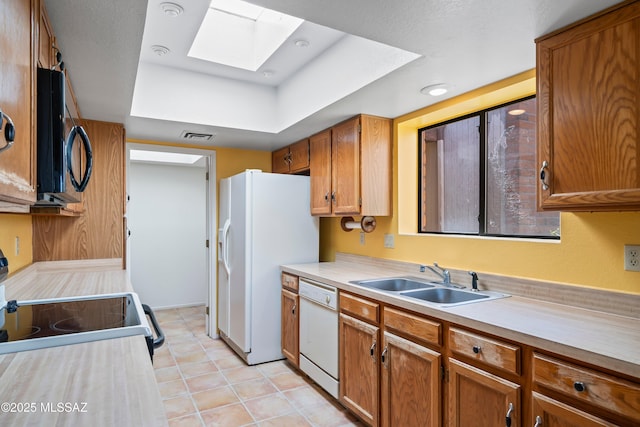 kitchen featuring a sink, a skylight, white appliances, brown cabinetry, and light countertops