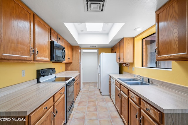 kitchen with black appliances, a tray ceiling, a sink, and light countertops