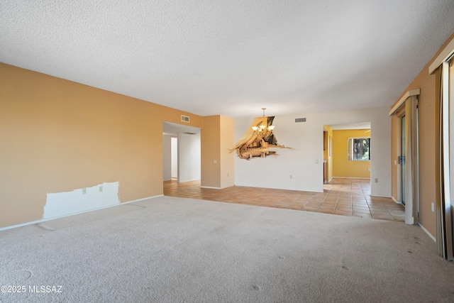 unfurnished room featuring a textured ceiling, a chandelier, light tile patterned floors, light colored carpet, and visible vents
