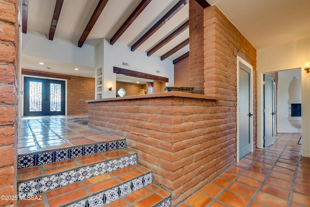 stairs with lofted ceiling with beams, french doors, brick wall, and tile patterned flooring