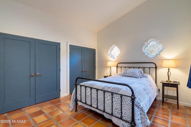 tiled bedroom with baseboards, two closets, and lofted ceiling