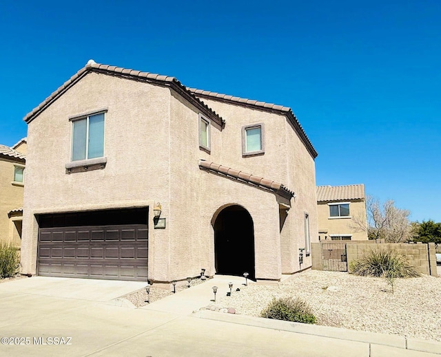 mediterranean / spanish house with stucco siding, fence, an attached garage, and a tile roof