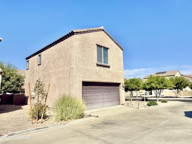 view of property exterior with an attached garage, concrete driveway, stucco siding, and a tile roof