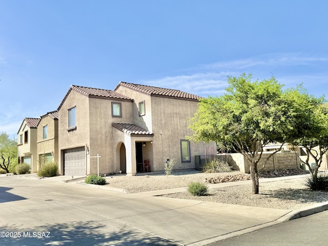 mediterranean / spanish-style home featuring stucco siding, driveway, an attached garage, a tiled roof, and fence