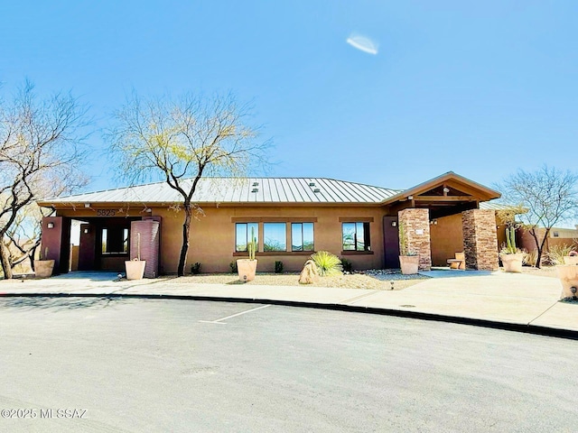 view of front facade with stone siding, metal roof, a standing seam roof, and stucco siding