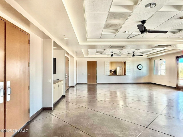 interior space with a raised ceiling, ceiling fan, baseboards, and tile patterned flooring