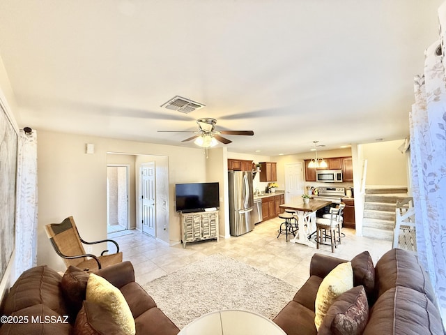 living area featuring light tile patterned flooring, ceiling fan, visible vents, and stairs