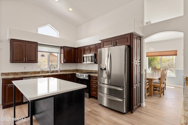kitchen with dark brown cabinetry, arched walkways, light countertops, high vaulted ceiling, and stainless steel appliances