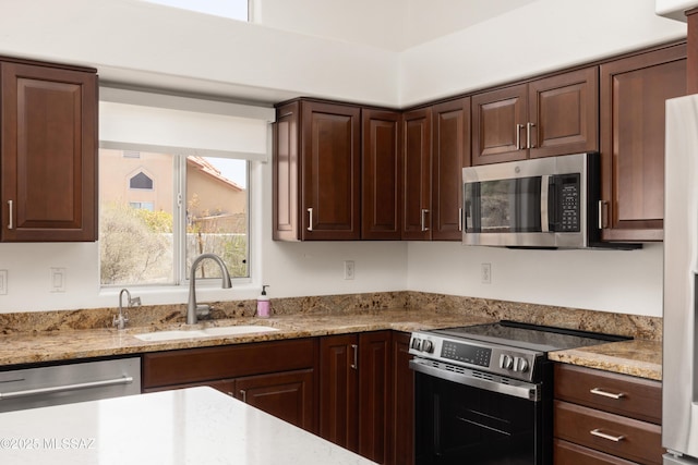 kitchen featuring a sink, appliances with stainless steel finishes, dark brown cabinetry, and light stone counters