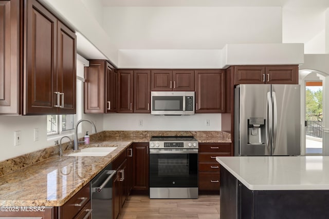 kitchen with arched walkways, light stone countertops, a sink, light wood-style floors, and stainless steel appliances