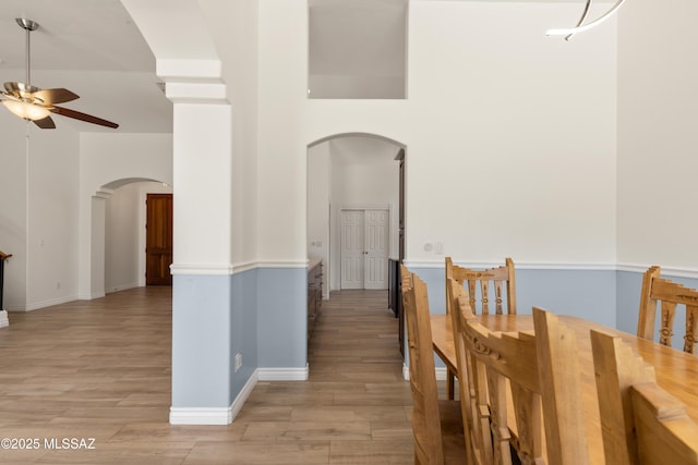 dining room with arched walkways, a ceiling fan, baseboards, and light wood-type flooring