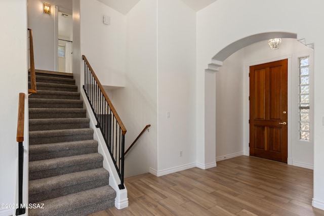 foyer with baseboards, arched walkways, stairs, and wood finished floors
