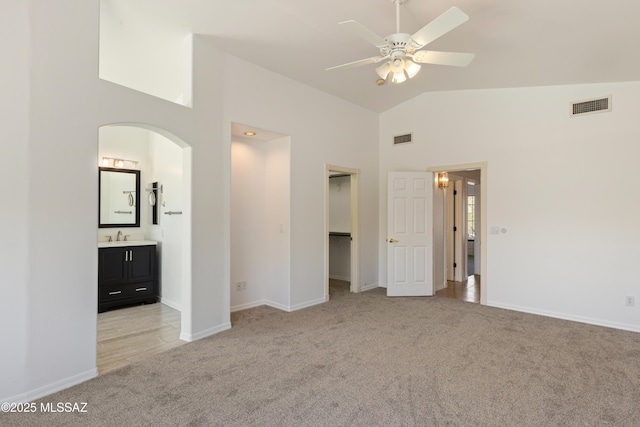 unfurnished bedroom featuring arched walkways, visible vents, high vaulted ceiling, and light colored carpet