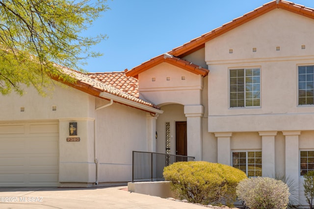mediterranean / spanish-style home with a garage, stucco siding, a tiled roof, and driveway