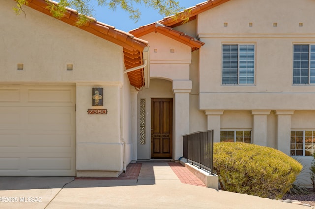 view of exterior entry featuring a garage, stucco siding, and concrete driveway