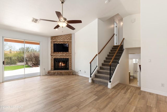 unfurnished living room featuring ceiling fan, visible vents, vaulted ceiling, stairs, and light wood-style flooring