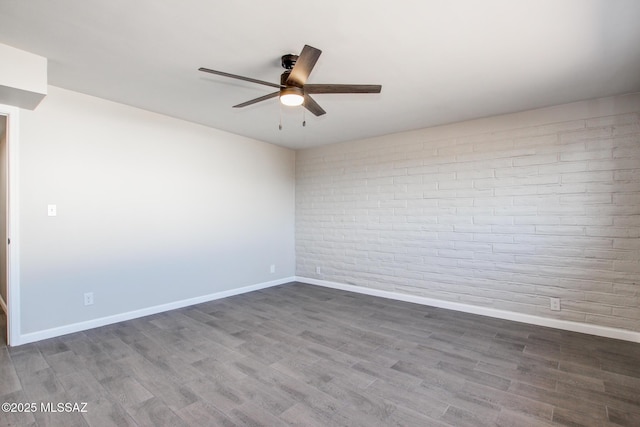 empty room featuring baseboards, brick wall, wood finished floors, and a ceiling fan
