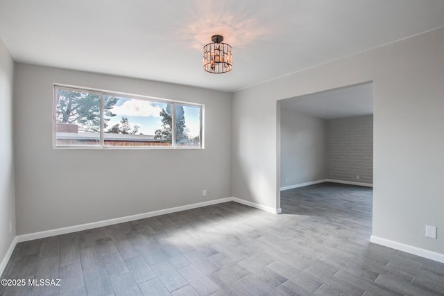 empty room with baseboards, an inviting chandelier, and wood finished floors