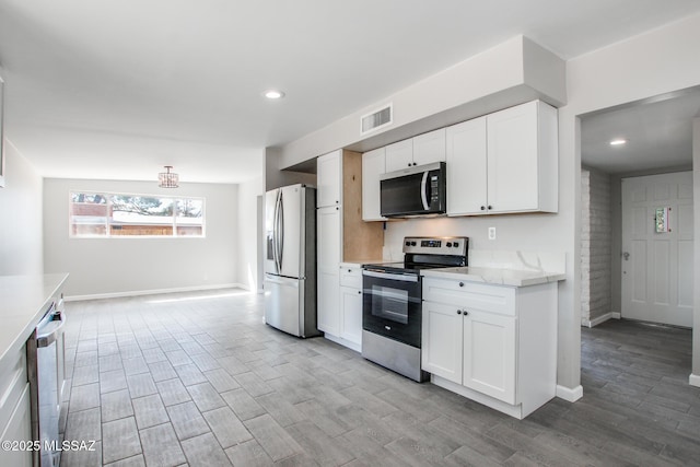 kitchen featuring visible vents, stainless steel appliances, white cabinets, light wood finished floors, and baseboards