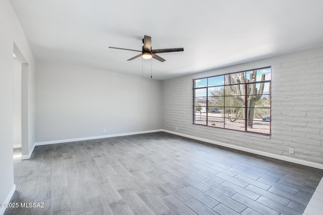 unfurnished room featuring brick wall, baseboards, a ceiling fan, and wood finished floors
