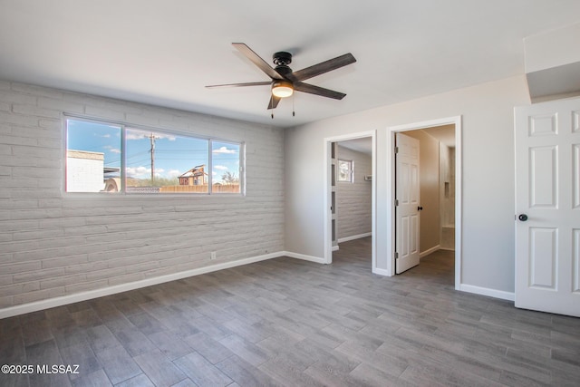 unfurnished bedroom with baseboards, a ceiling fan, wood finished floors, and brick wall