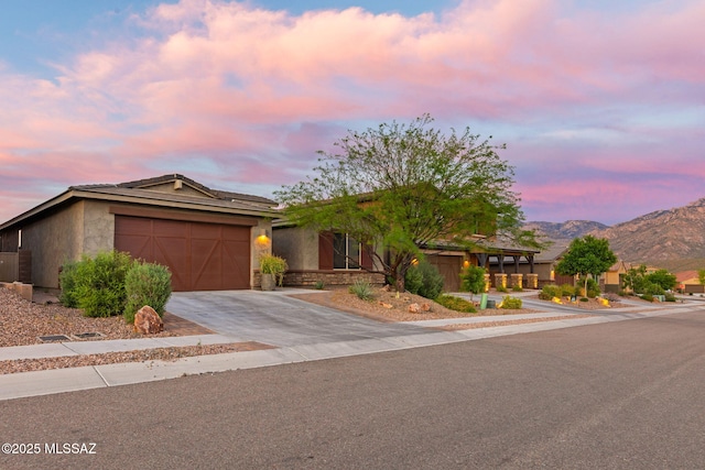 view of front of home featuring stucco siding, concrete driveway, a garage, stone siding, and a mountain view