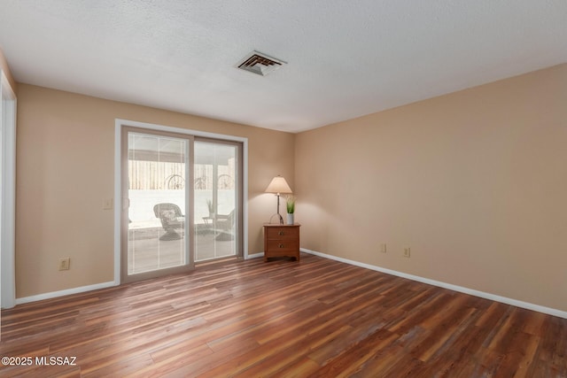 spare room featuring visible vents, a textured ceiling, baseboards, and wood finished floors