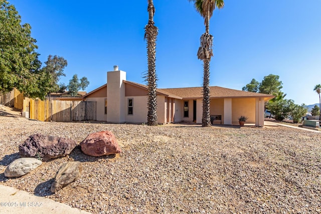 back of house with stucco siding, a chimney, and fence