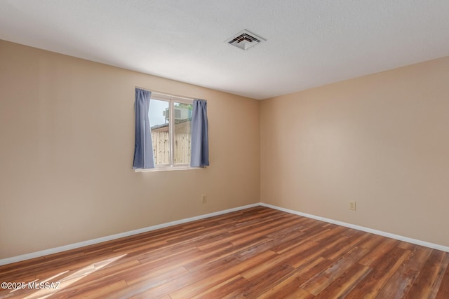 empty room featuring a textured ceiling, wood finished floors, visible vents, and baseboards