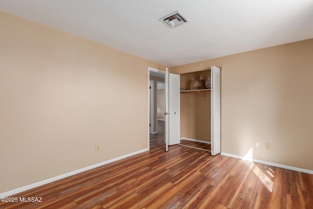 unfurnished bedroom featuring visible vents, a textured ceiling, wood finished floors, a closet, and baseboards