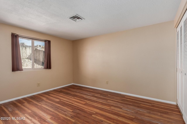 empty room with a textured ceiling, wood finished floors, visible vents, and baseboards