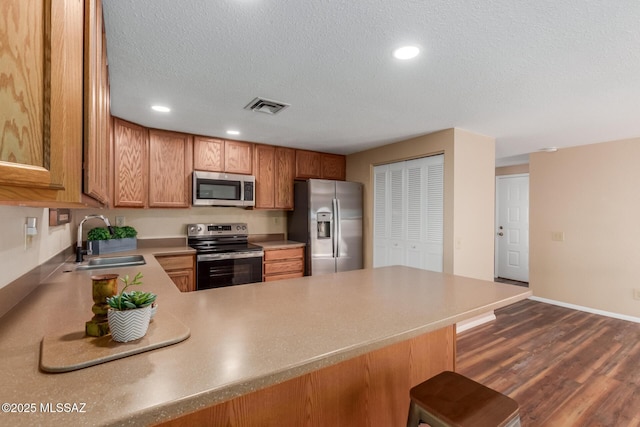 kitchen with visible vents, a sink, stainless steel appliances, a peninsula, and dark wood-style flooring