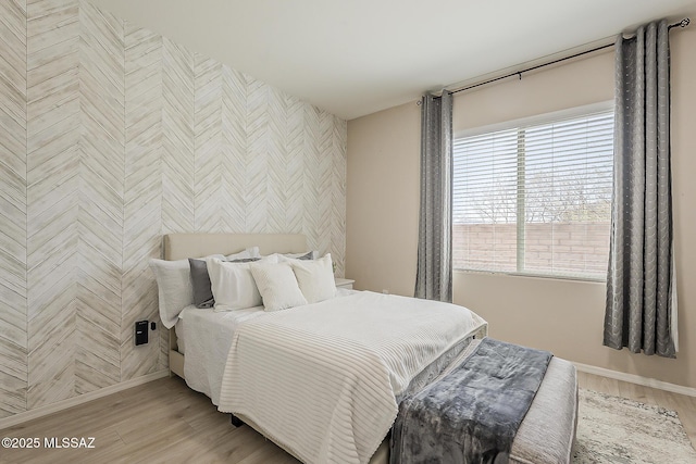 bedroom with baseboards, an accent wall, and light wood-style floors