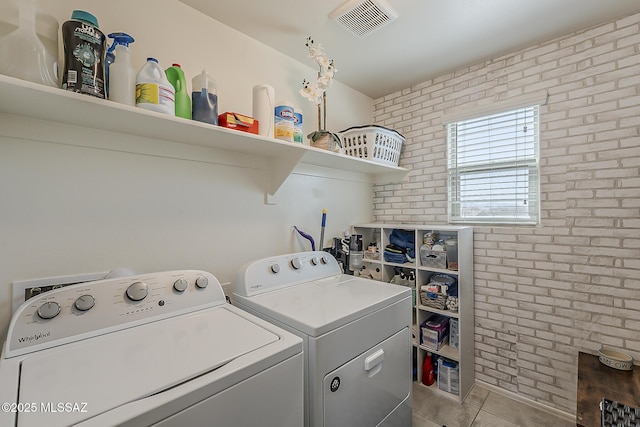 laundry room featuring visible vents, brick wall, washer and clothes dryer, laundry area, and tile patterned floors