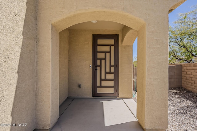 doorway to property featuring stucco siding and fence