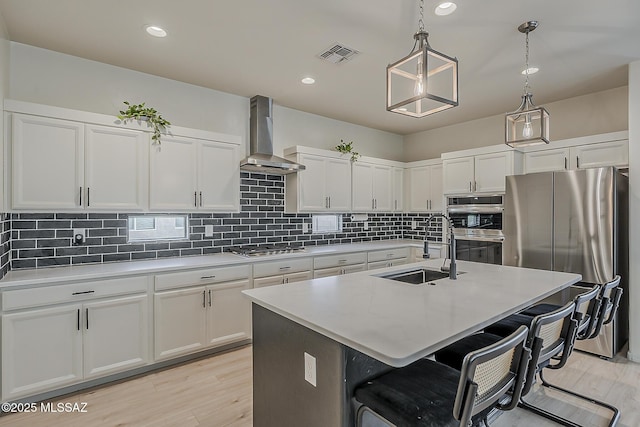 kitchen with visible vents, a breakfast bar, a sink, stainless steel appliances, and wall chimney range hood