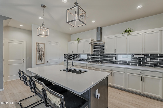 kitchen featuring stainless steel gas cooktop, light countertops, wall chimney exhaust hood, and a sink