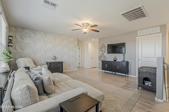 living area with visible vents, an accent wall, and a ceiling fan