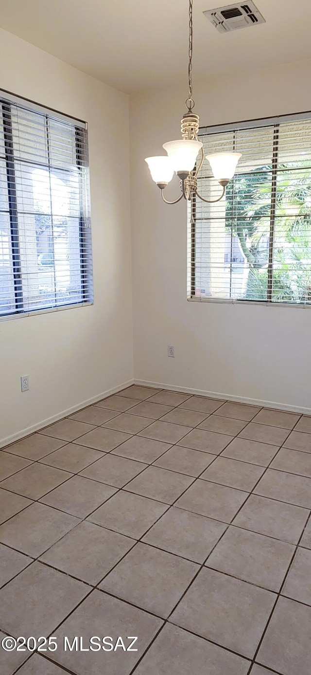 empty room featuring baseboards, visible vents, a chandelier, and light tile patterned floors