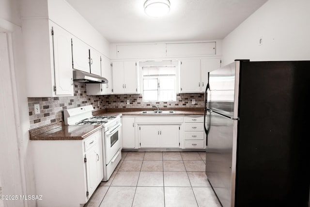 kitchen with under cabinet range hood, dark countertops, white gas range oven, freestanding refrigerator, and light tile patterned flooring