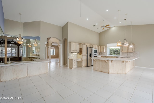 kitchen with high vaulted ceiling, light brown cabinets, decorative backsplash, stainless steel fridge with ice dispenser, and light countertops