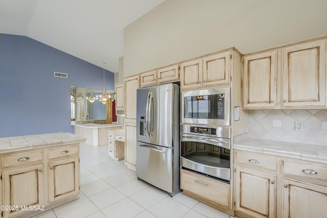 kitchen featuring lofted ceiling, decorative backsplash, appliances with stainless steel finishes, light brown cabinets, and light tile patterned floors