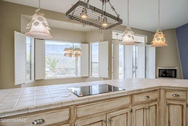 kitchen featuring black electric cooktop, an inviting chandelier, light brown cabinets, a fireplace, and hanging light fixtures